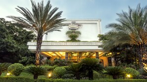 A building with a white facade, a central decorative element, and a garden with various plants and trees. - Taj Deccan (Hyderabad)