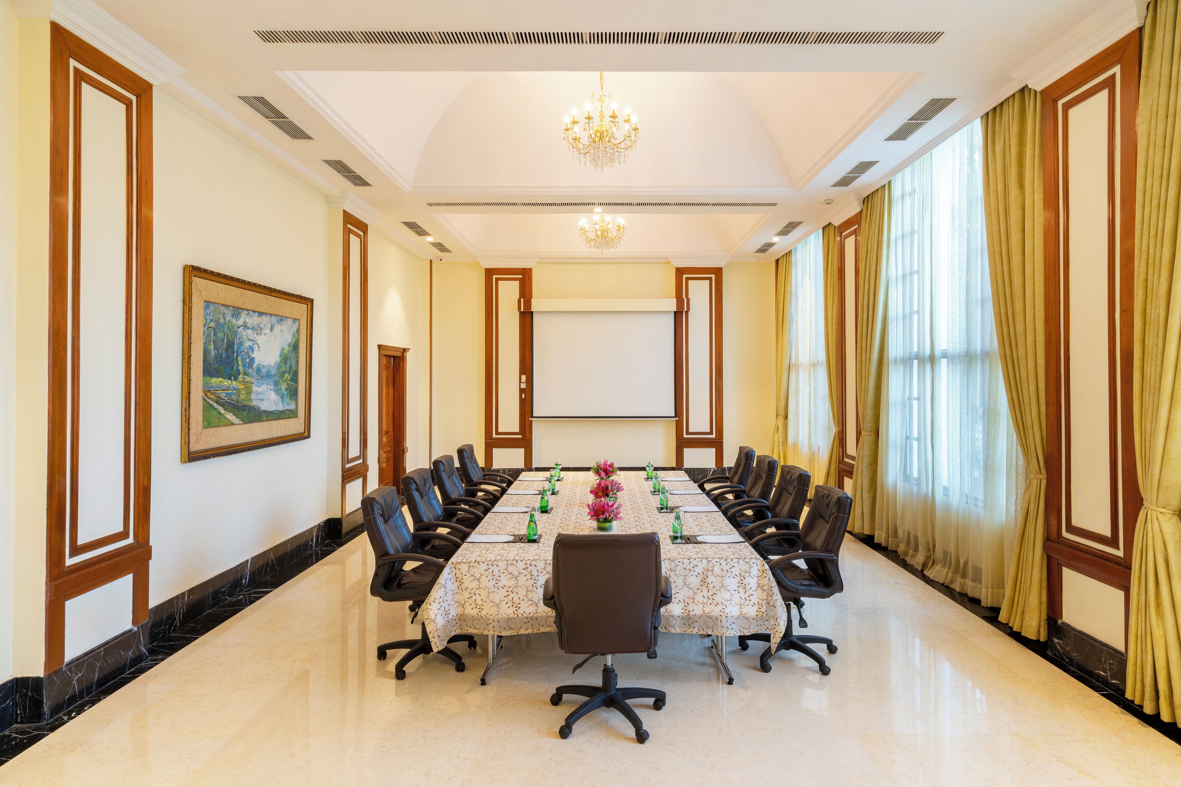 Une salle de conférence avec une longue table, des chaises, un écran de projection et un lustre.