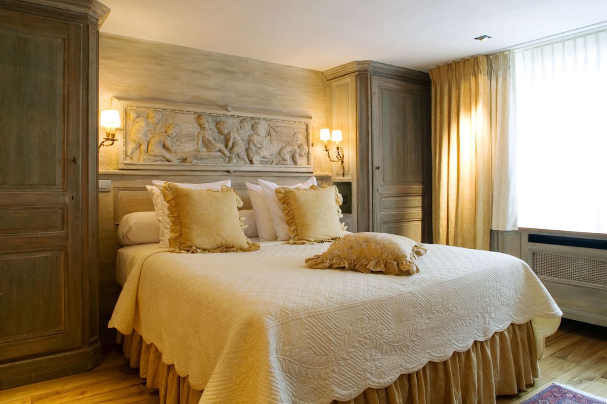 A large bed with a decorative headboard, multiple pillows, and a light-colored quilt.