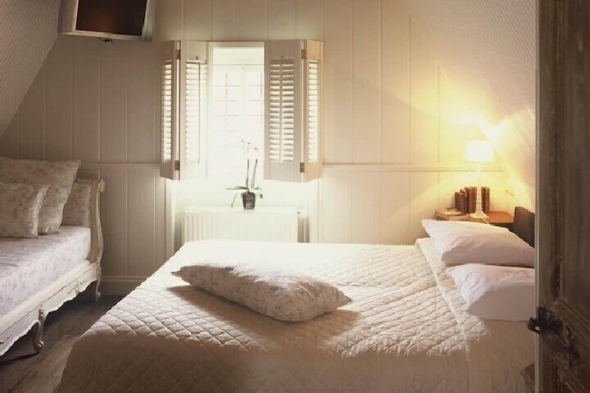 A bedroom with a large bed, a TV mounted on the wall, and a chandelier.