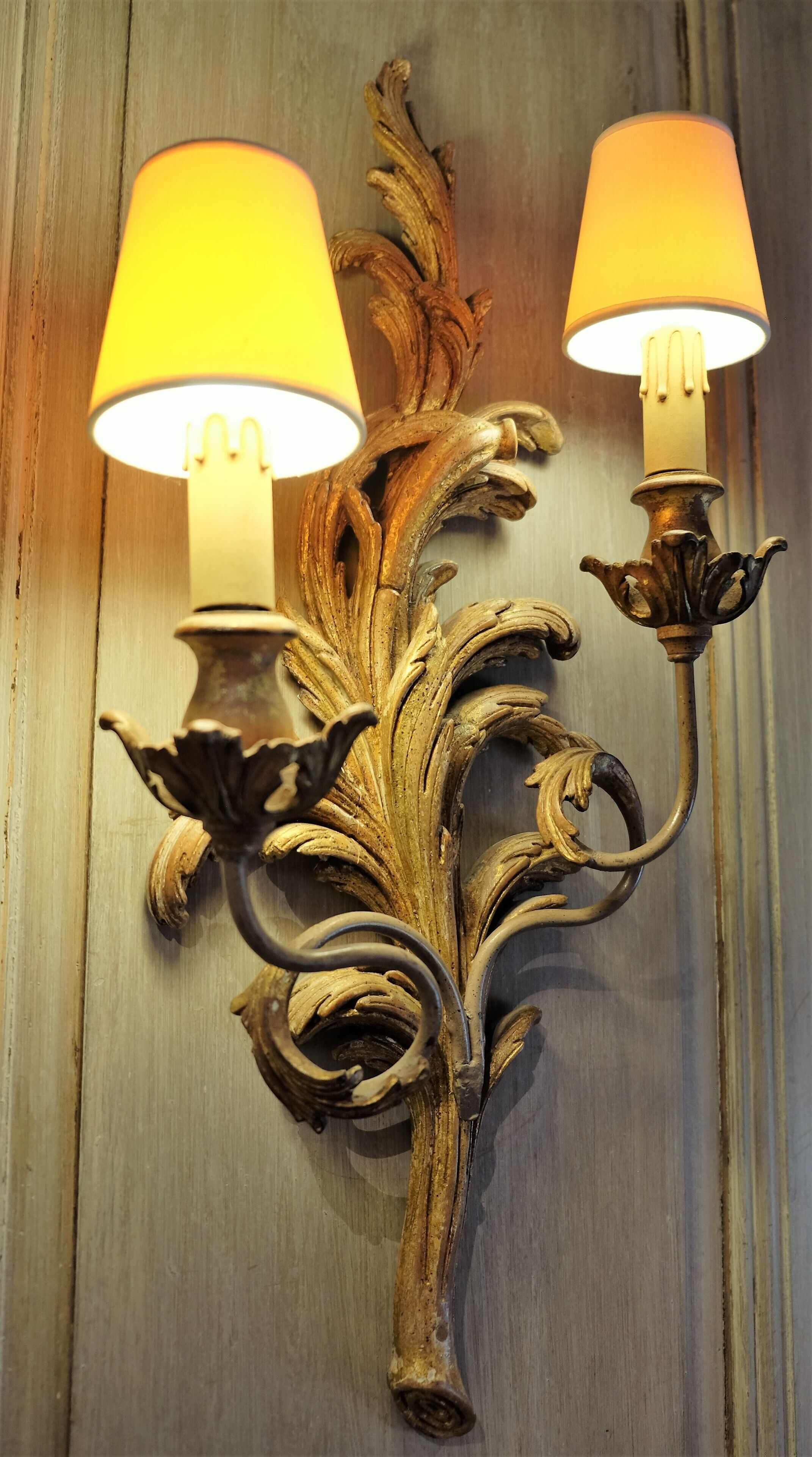 Eine wandmontierte Leuchte mit zwei Lampen, verziert mit aufwendigen, blattartigen Ornamenten.