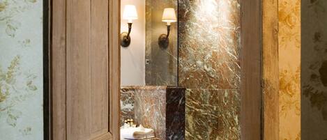 Un baño con pared de mármol, puerta de madera y un espejo.