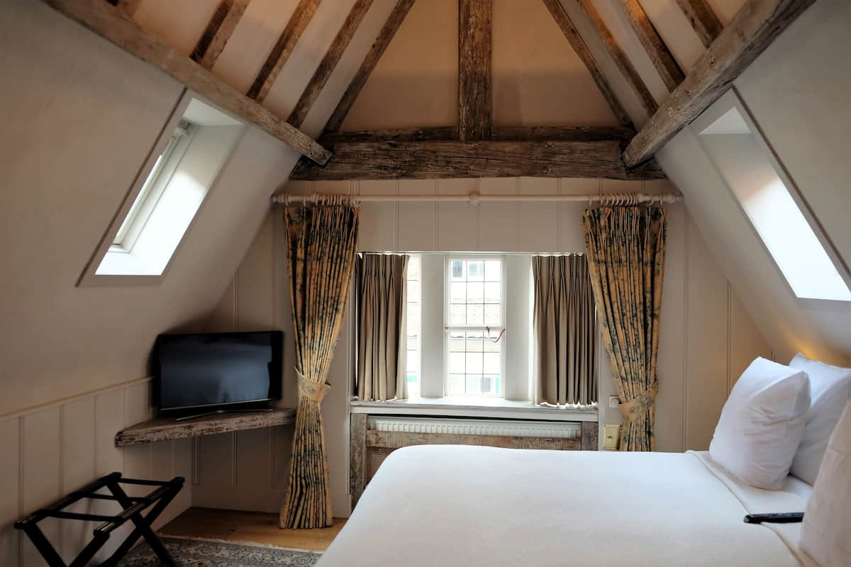 A bedroom with a sloped ceiling, a bed, a television on a shelf, and a window with curtains.