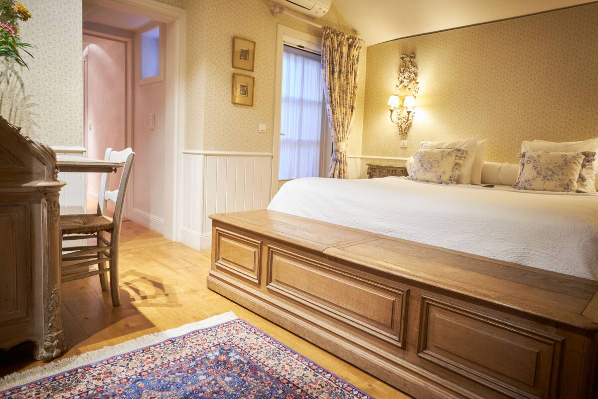 A bedroom with a large bed, a wooden dresser, a chair, a desk, and a patterned rug.