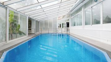 An indoor swimming pool with clear glass walls, a tiled floor, and a glass ceiling.