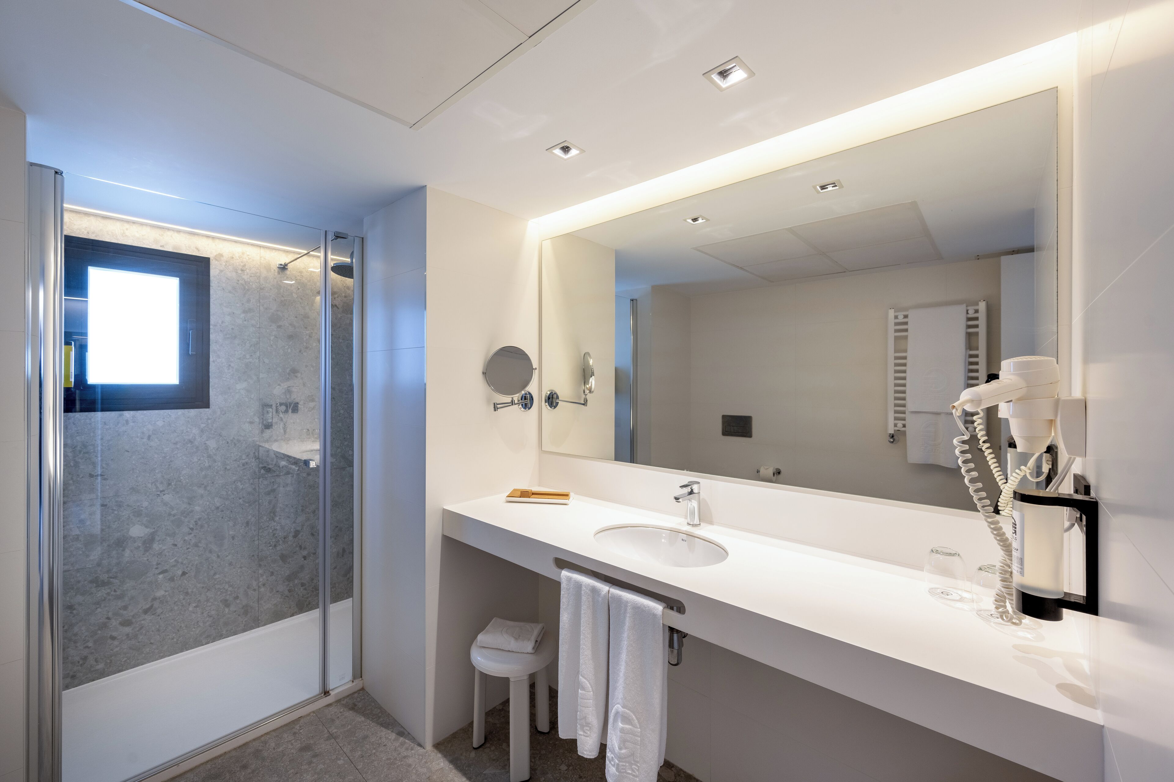 A modern bathroom with a glass shower enclosure, a large mirror, and a white sink.