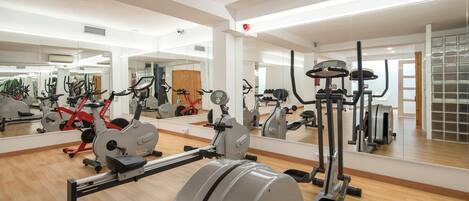 Un gimnasio con diversos equipos de ejercicio, incluyendo una máquina de remo, una elíptica y una bicicleta estática.