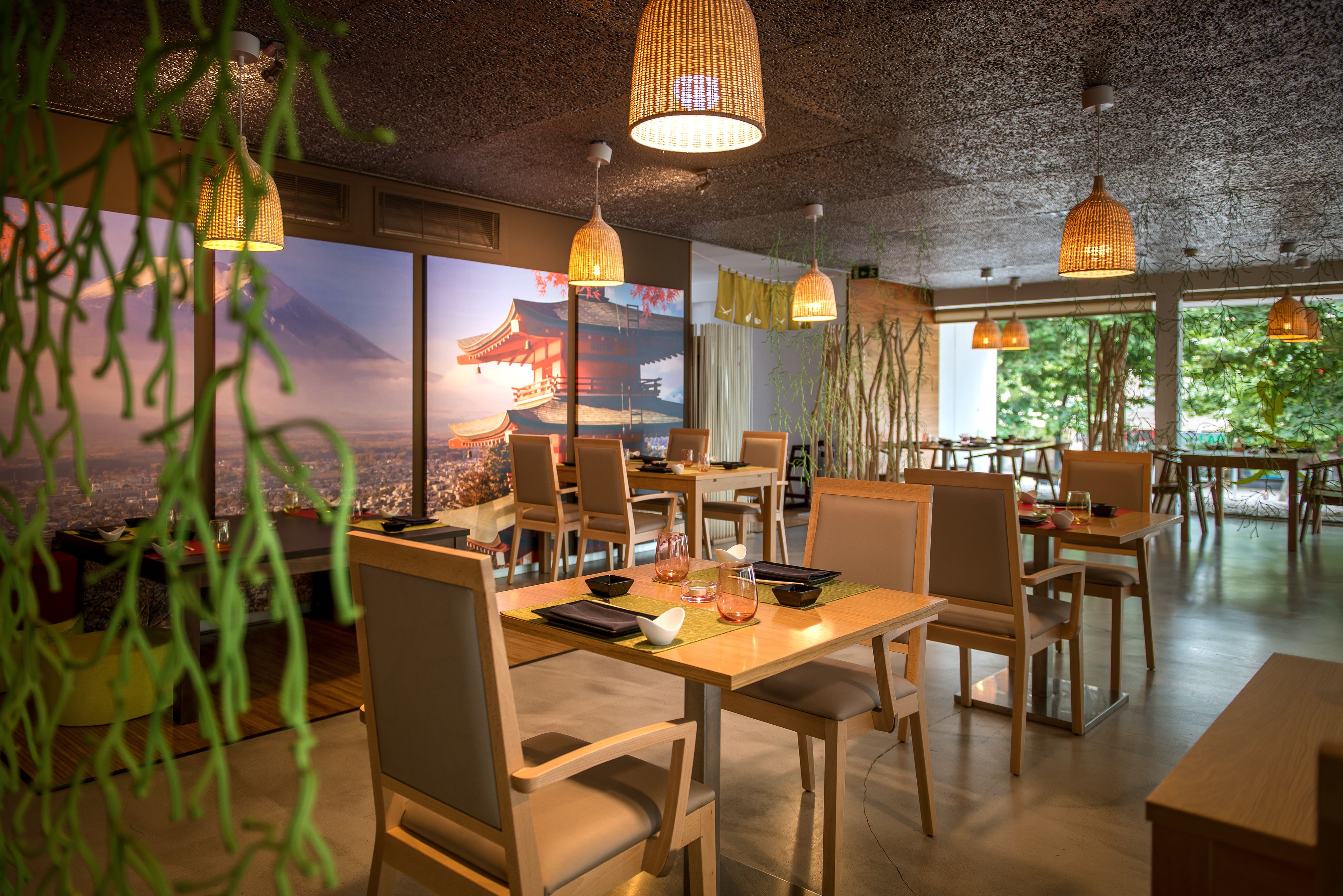 A restaurant with wooden tables and chairs, hanging pendant lights, and a large window with a view of a mountain.
