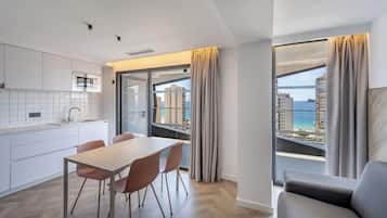 Een moderne keuken met een eethoek, grote ramen voorzien van gordijnen en uitzicht op zee en gebouwen.