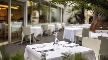 Een restaurant met witte tafellakens, keurig gedekte tafels en een palmboom op de achtergrond.