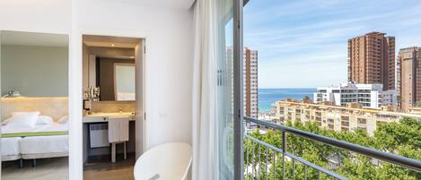 Una habitación de hotel moderna con balcón, cama, baño y vistas a la ciudad y al mar.