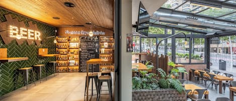 A modern bar area with a wooden ceiling, a green wall with a 'BEER' sign, and a variety of bottles on shelves.