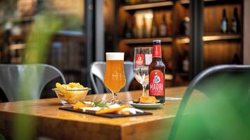 Une table avec un bol de chips, un verre de bière, une bouteille de bière Madri et un verre d’eau.