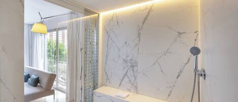 Un baño moderno con pared de mármol, banco integrado, ducha y vistas al exterior.