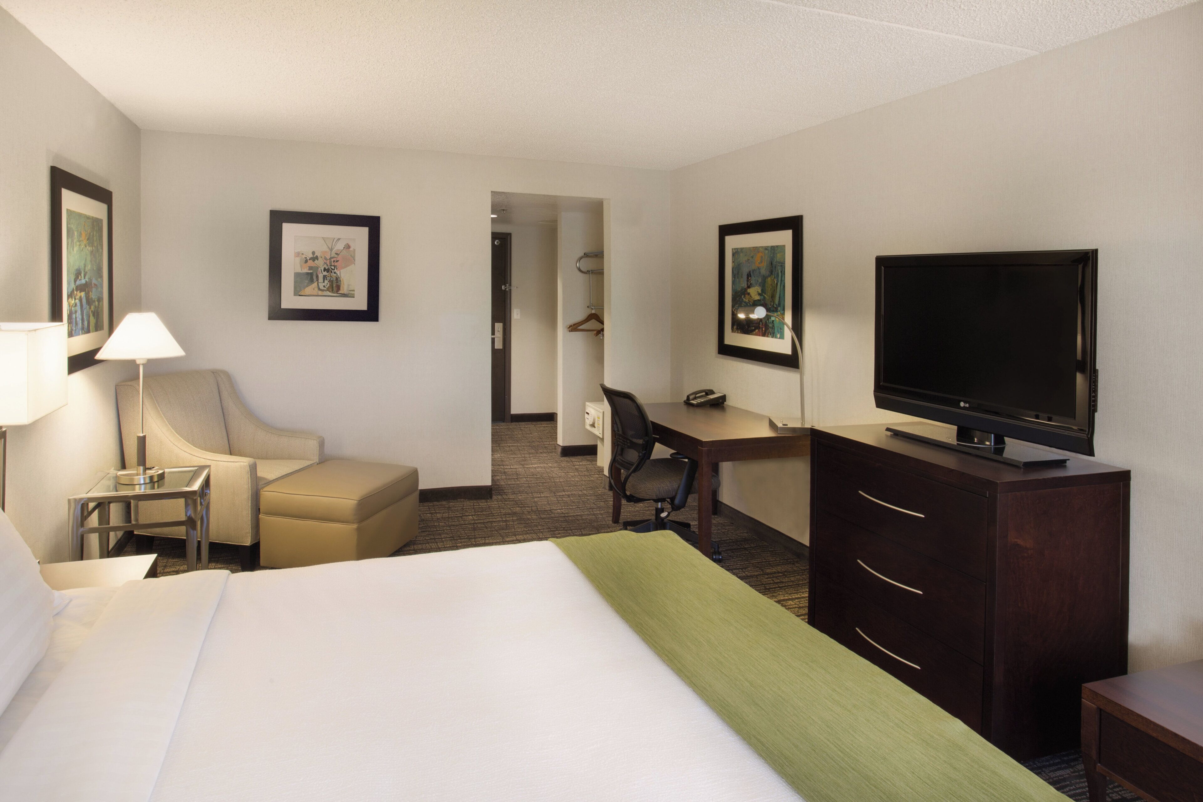 A hotel room with a bed, a desk, a chair, a television, and a lamp.