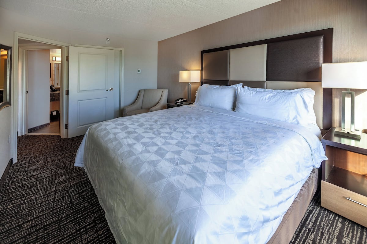 Une chambre d’hôtel avec un grand lit, une chaise, une table de chevet et une porte donnant sur une salle de bain.