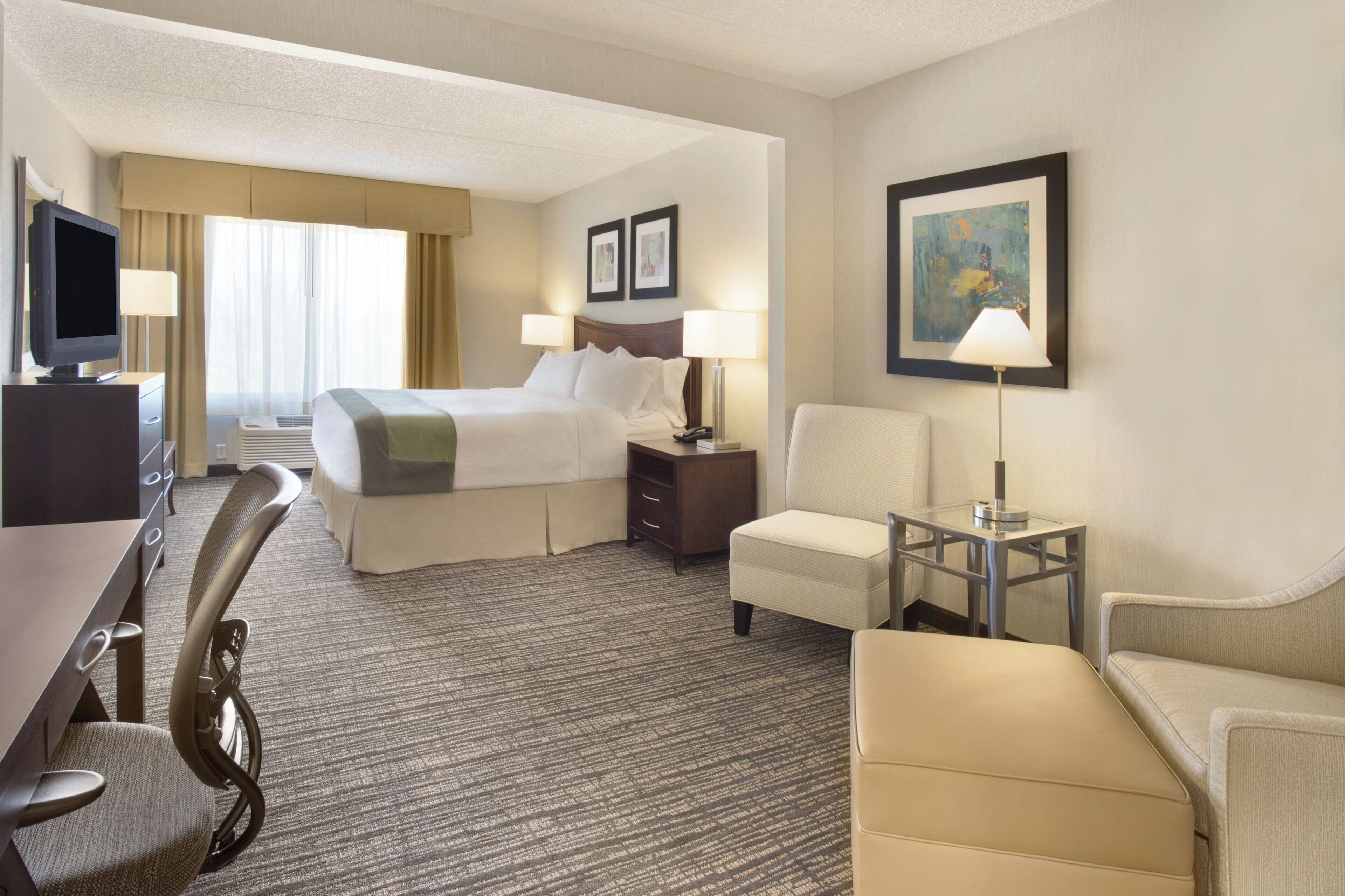 A hotel room with a bed, two bedside tables, a desk with a chair, a TV, and a lamp.
