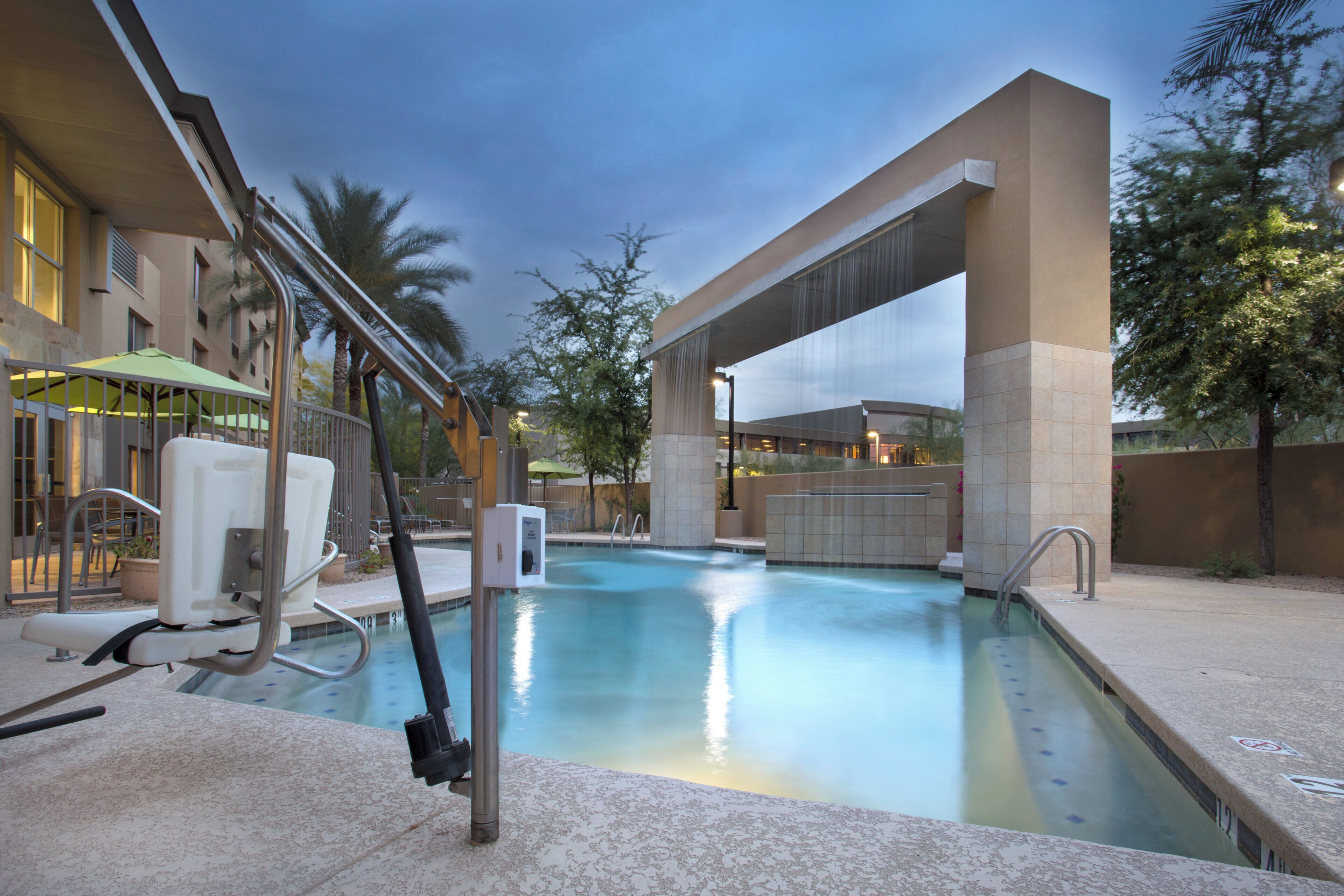 A swimming pool with a water slide, a sun lounger, and a covered seating area.