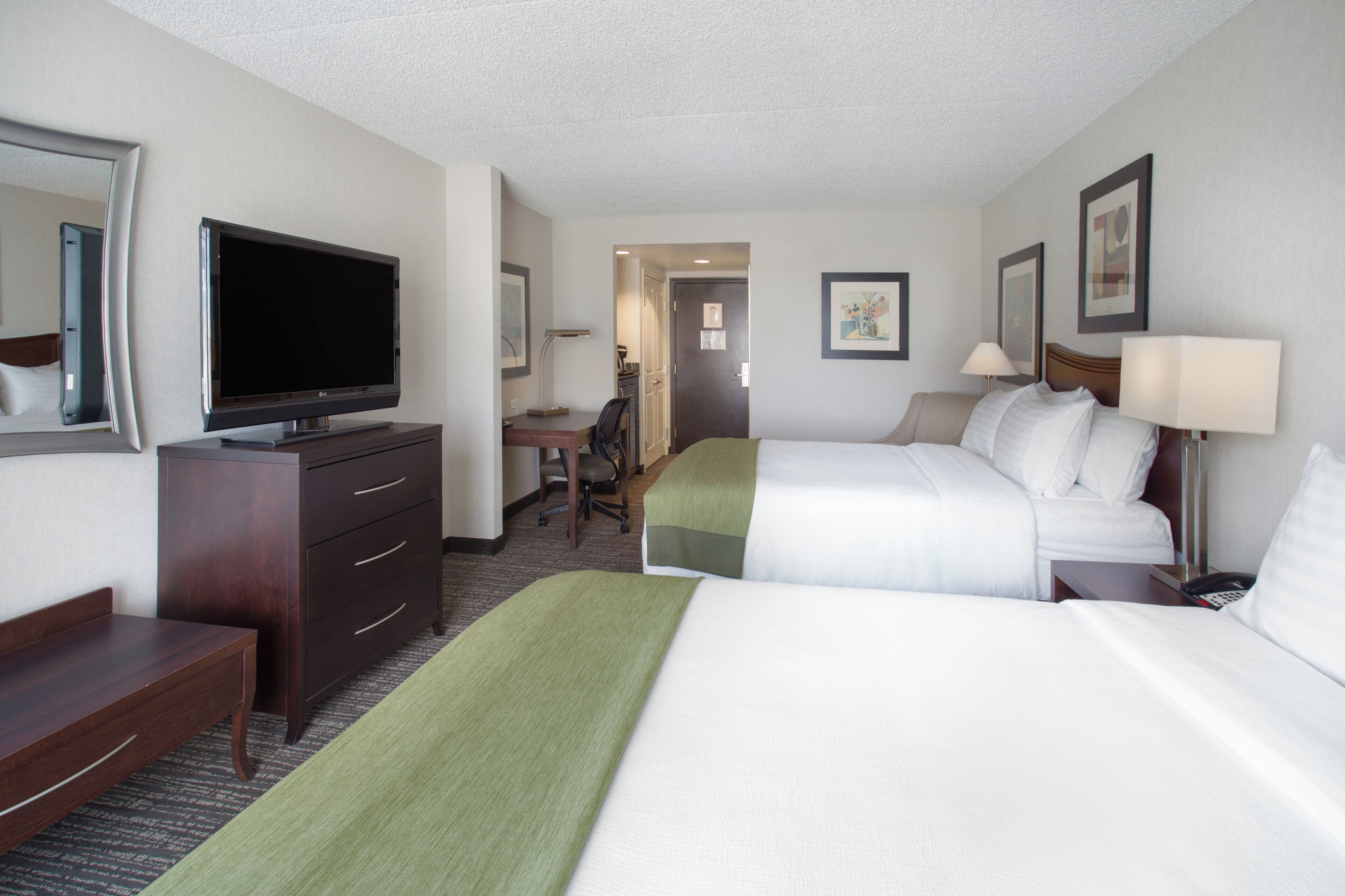A hotel room with two beds, a desk, a television, and a chair.