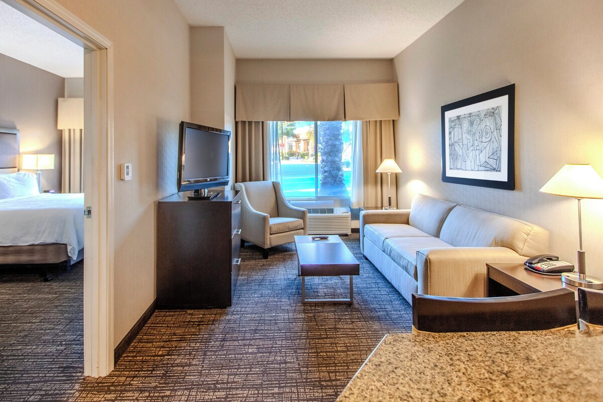 Een hotelkamer met een bed, een bureau met een televisie, een bank, een bijzettafeltje en uitzicht op de straat.