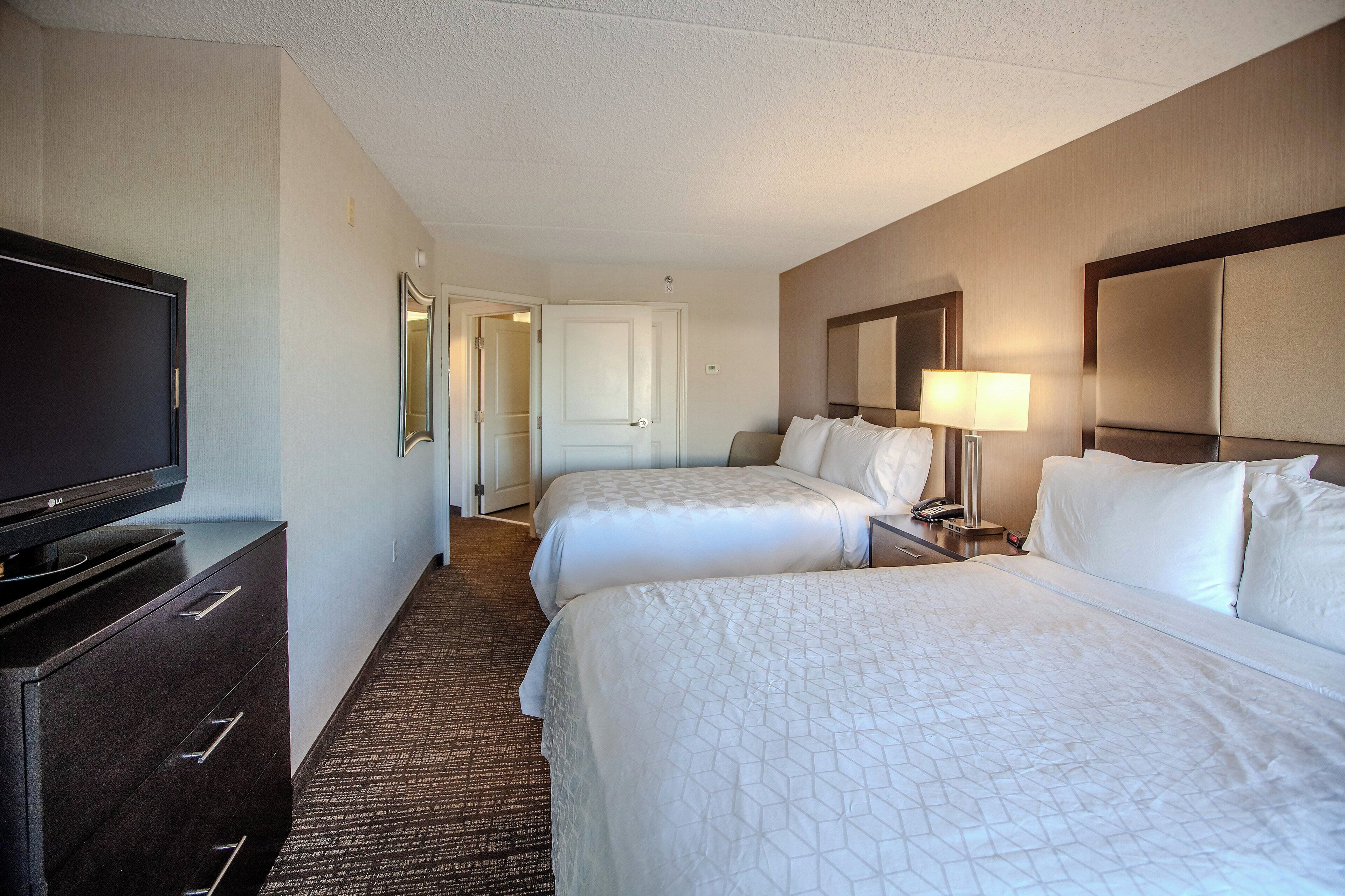 A hotel room with two beds, a TV, a dresser, a mirror, and a lamp.