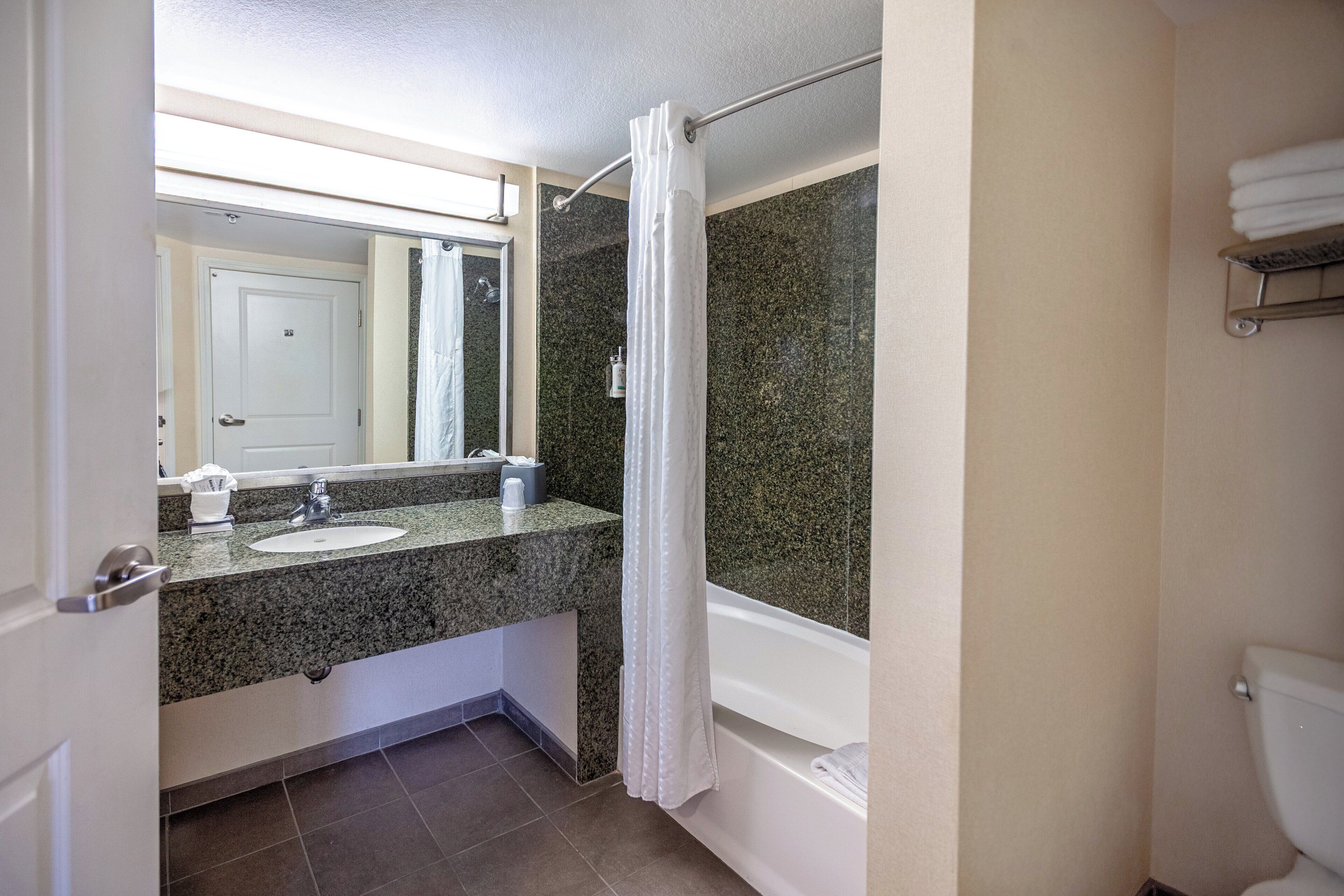 A bathroom with a granite countertop sink, a mirror, a shower curtain, a bathtub, and a toilet.