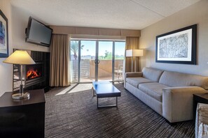 Hotelkamer met flatscreen televisie, open haard, bank, bijzettafeltje en een groot raam met uitzicht.