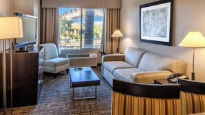 A hotel room with a sofa, a chair, a desk with a television, a lamp, and a framed artwork on the wall. - Holiday Inn & Suites Scottsdale North - Airpark by IHG (Scottsdale)