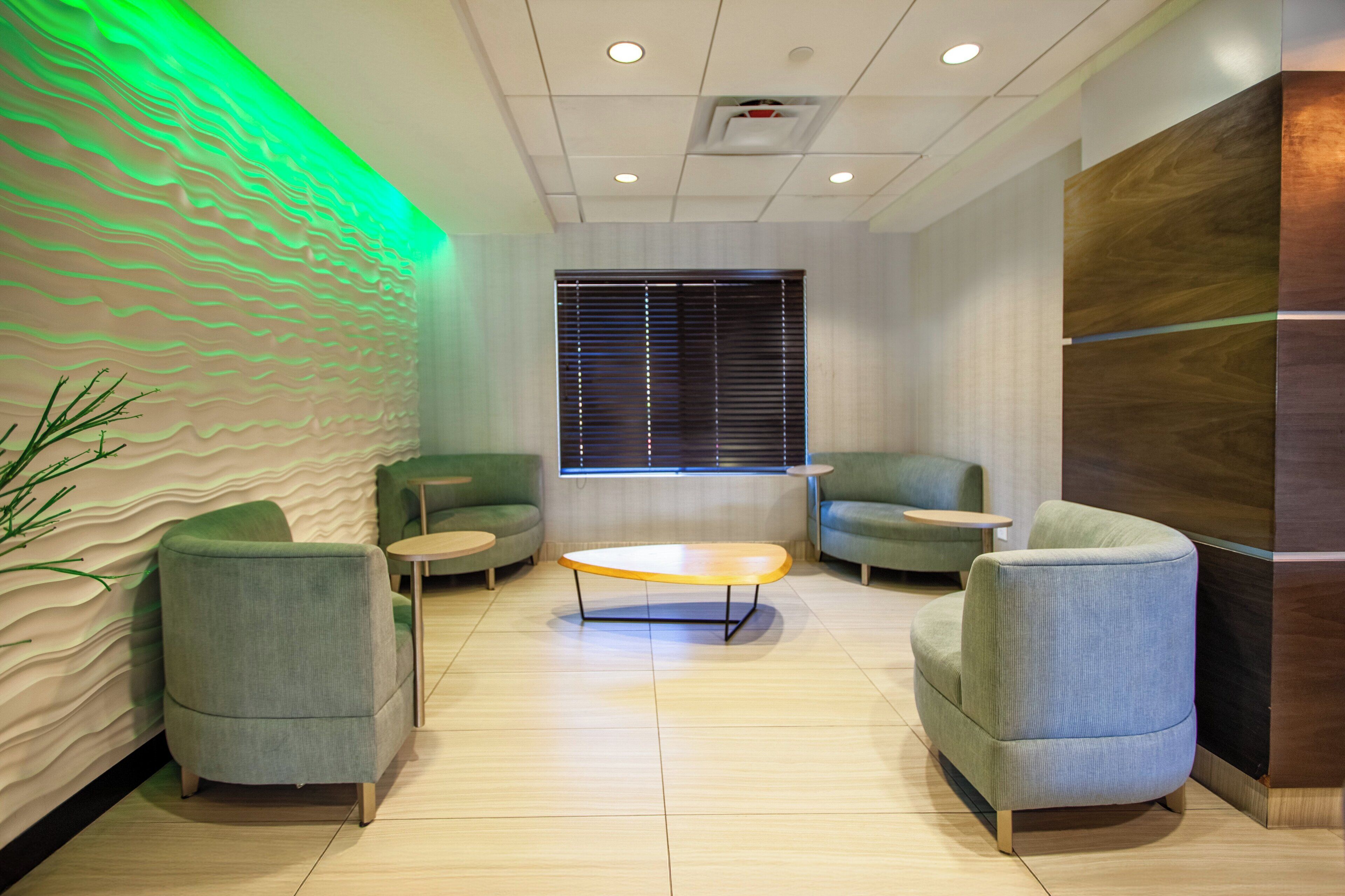 A modern lounge area with green upholstered chairs, a round coffee table, and a textured wall.