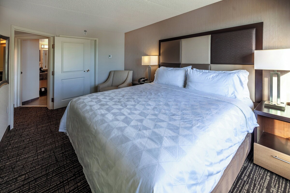 Een hotelkamer met een groot bed, een stoel, een nachtkastje en een deur naar een badkamer.