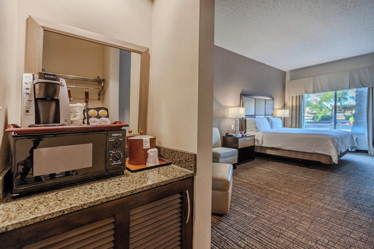 Une chambre d’hôtel équipée d’une kitchenette, d’un lit, d’un coin salon et d’une fenêtre donnant sur un paysage agréable.