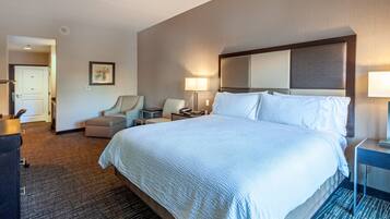 A hotel room with a large bed, two bedside tables, a desk, a chair, and a door.