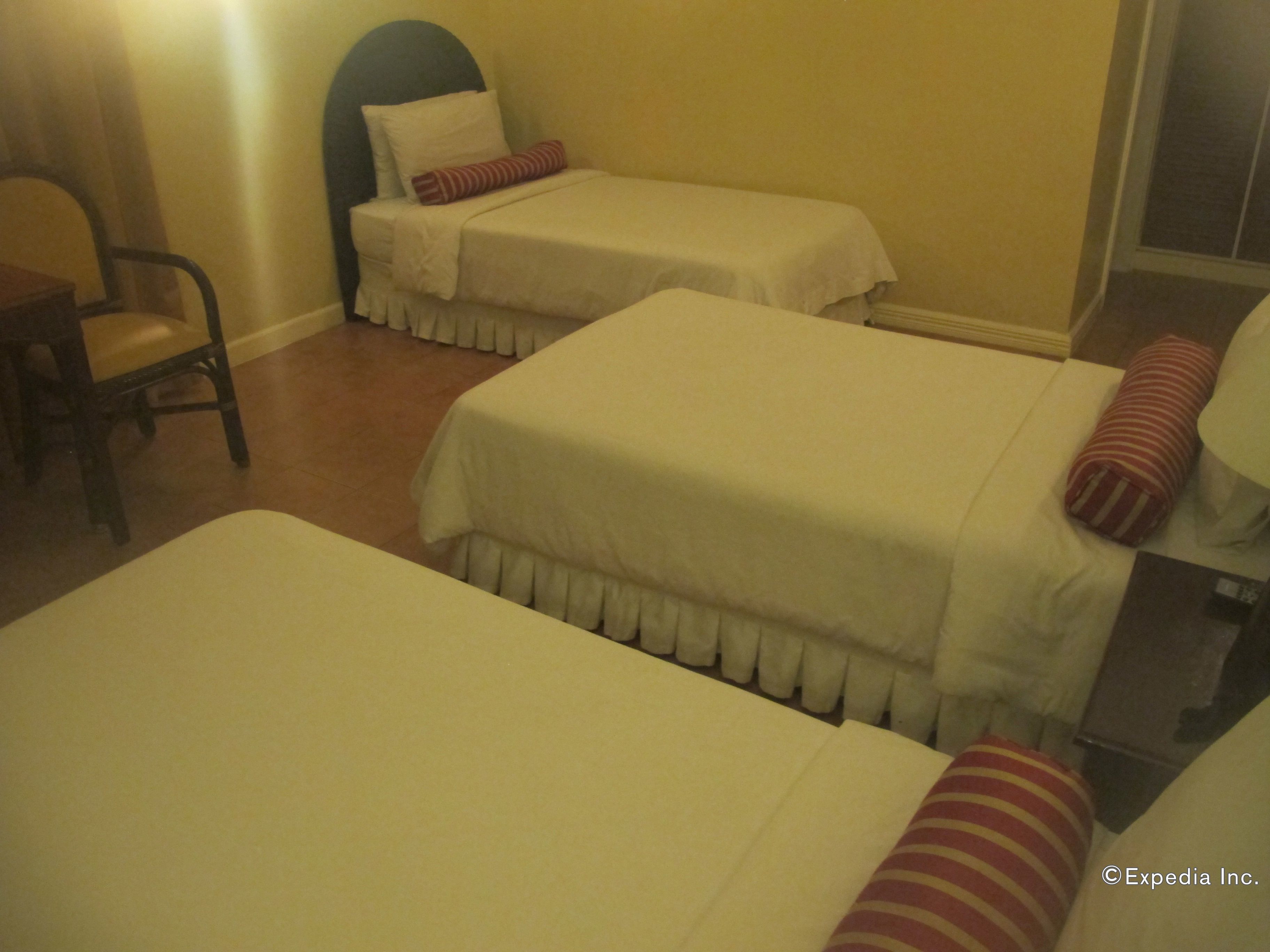 A hotel room with two beds, each with a white bedspread and a red-striped pillow. There is a chair and a small table in the room.