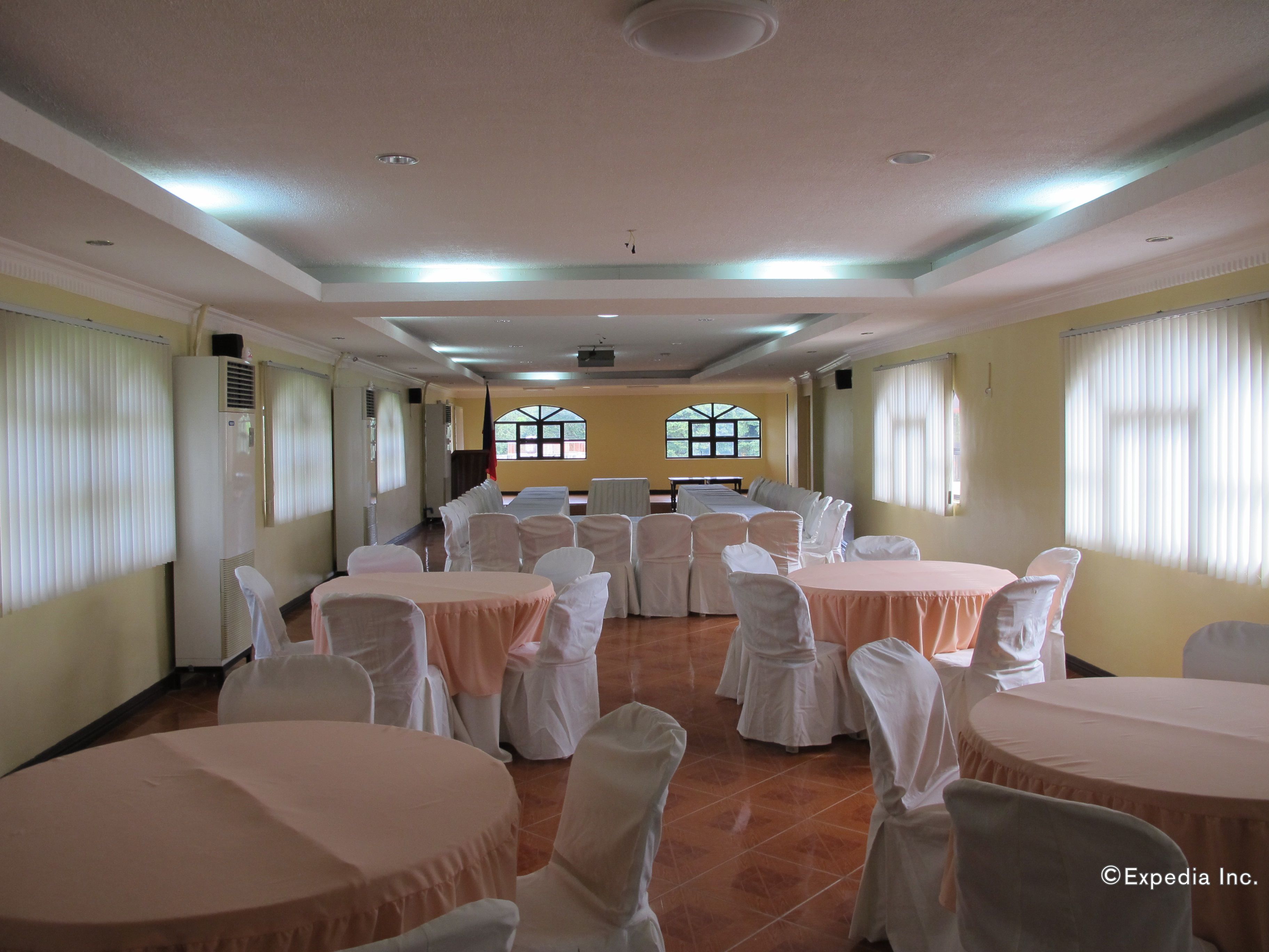 A banquet hall with round tables and chairs, large windows, and a ceiling with recessed lighting.