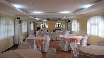 A banquet hall with round tables and chairs, large windows, and a ceiling with recessed lighting.