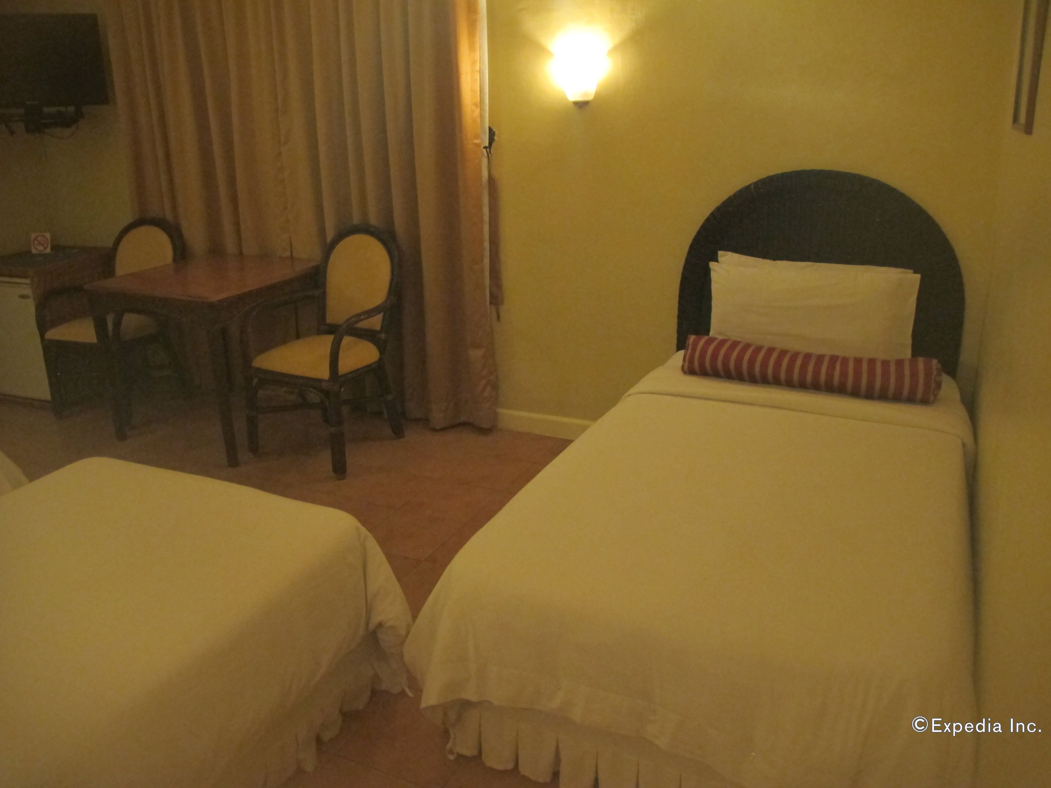A hotel room with two single beds, a desk, a chair, and a television.