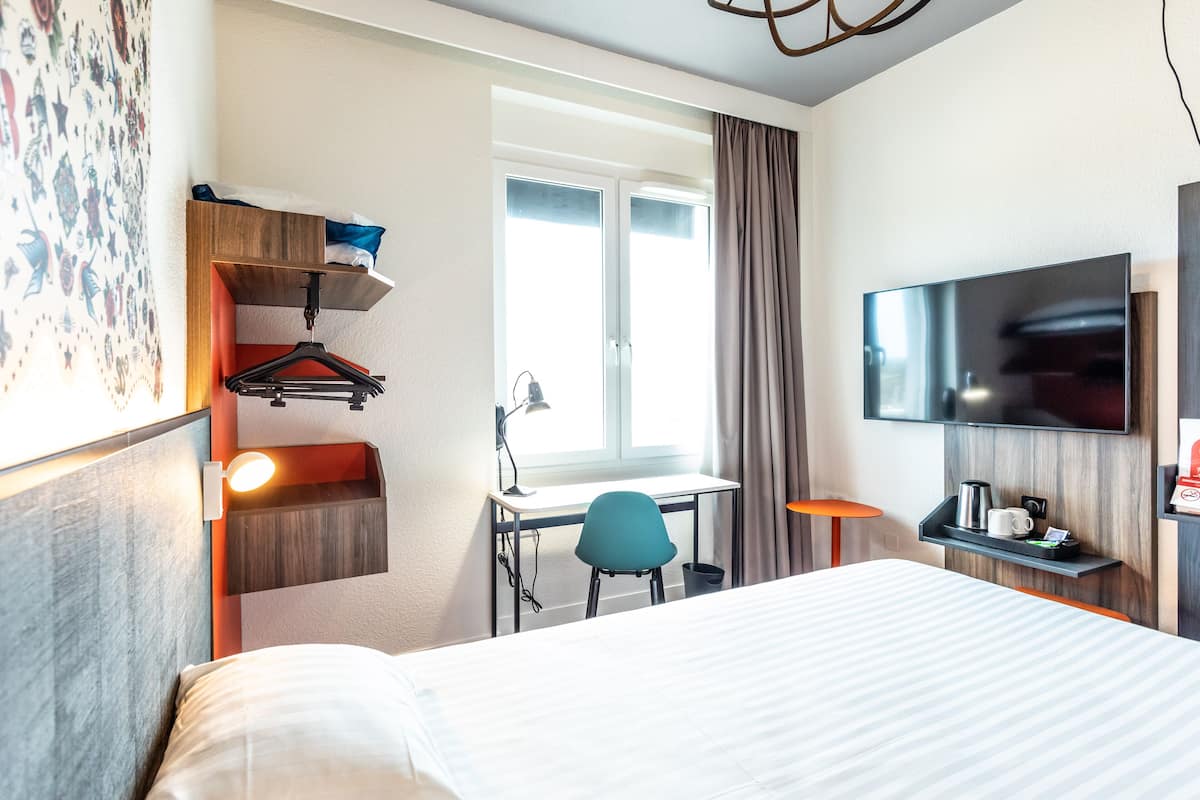 A hotel room with a bed, desk, chair, TV, and a window with curtains.
