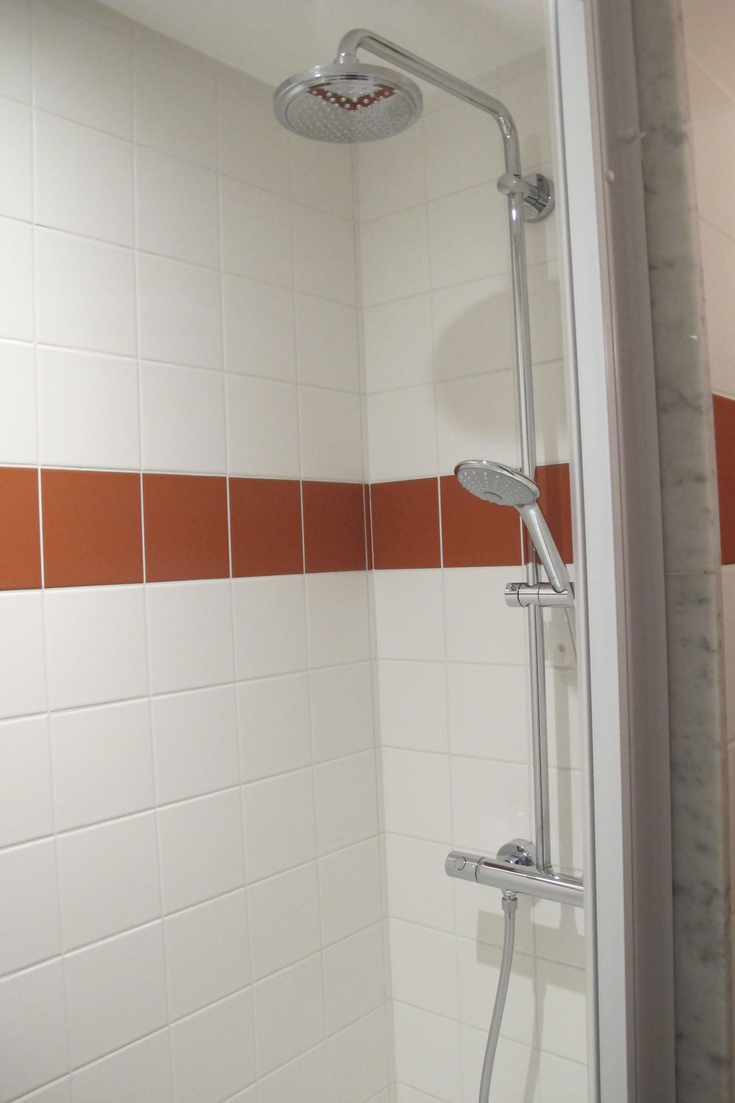 Une douche équipée d’un pommeau de douche à main et d’un robinet fixé au mur.