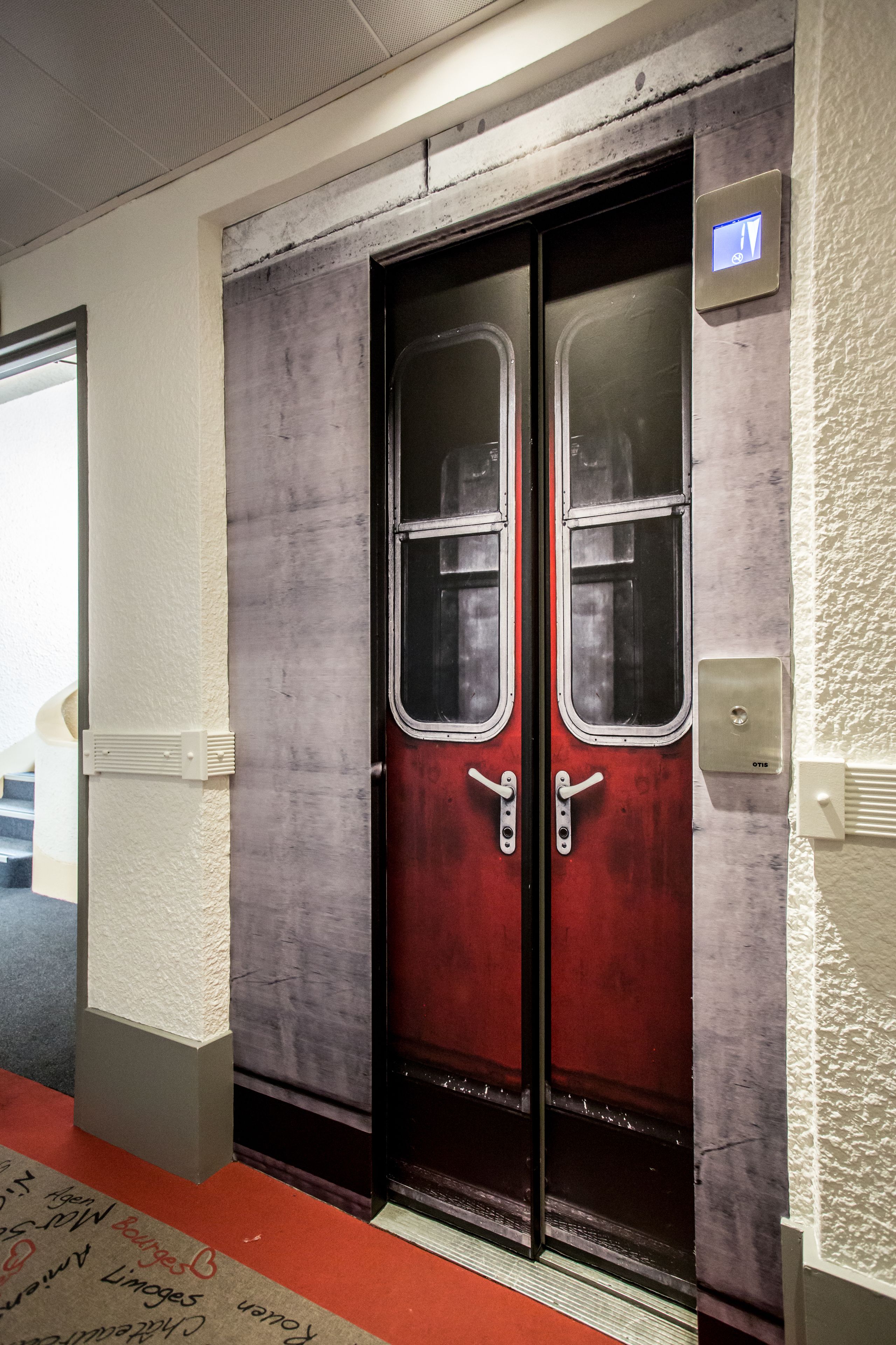 A red elevator with a metallic handle and a small illuminated sign above it.