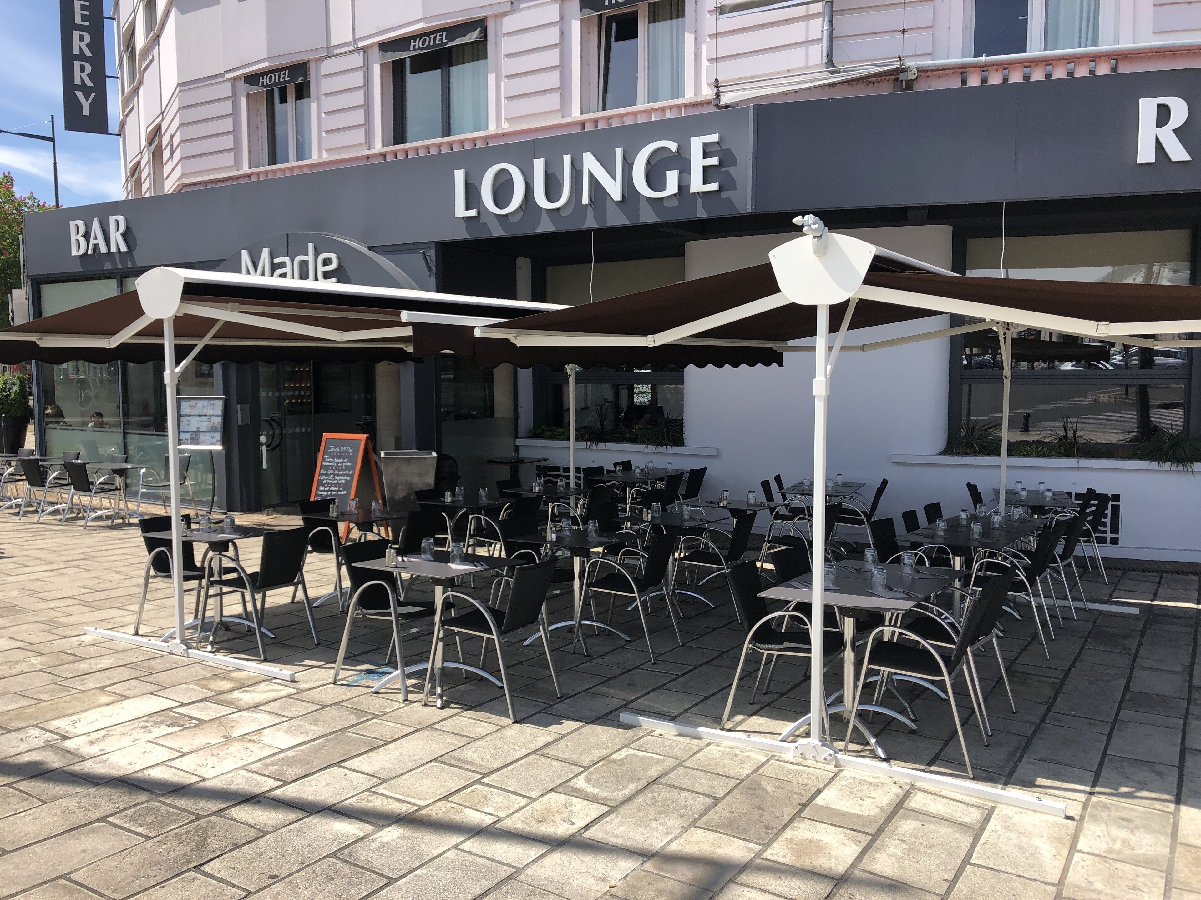 Un espacio al aire libre con mesas, sillas, una barra y un cartel que indica zona de lounge.