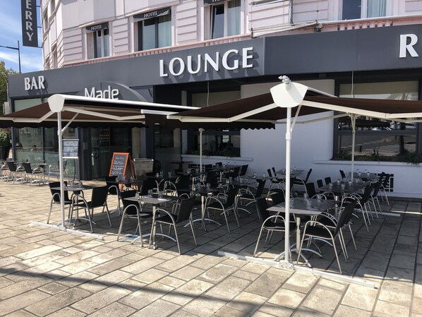 Un espacio al aire libre con mesas, sillas, una barra y un cartel que indica zona de lounge.