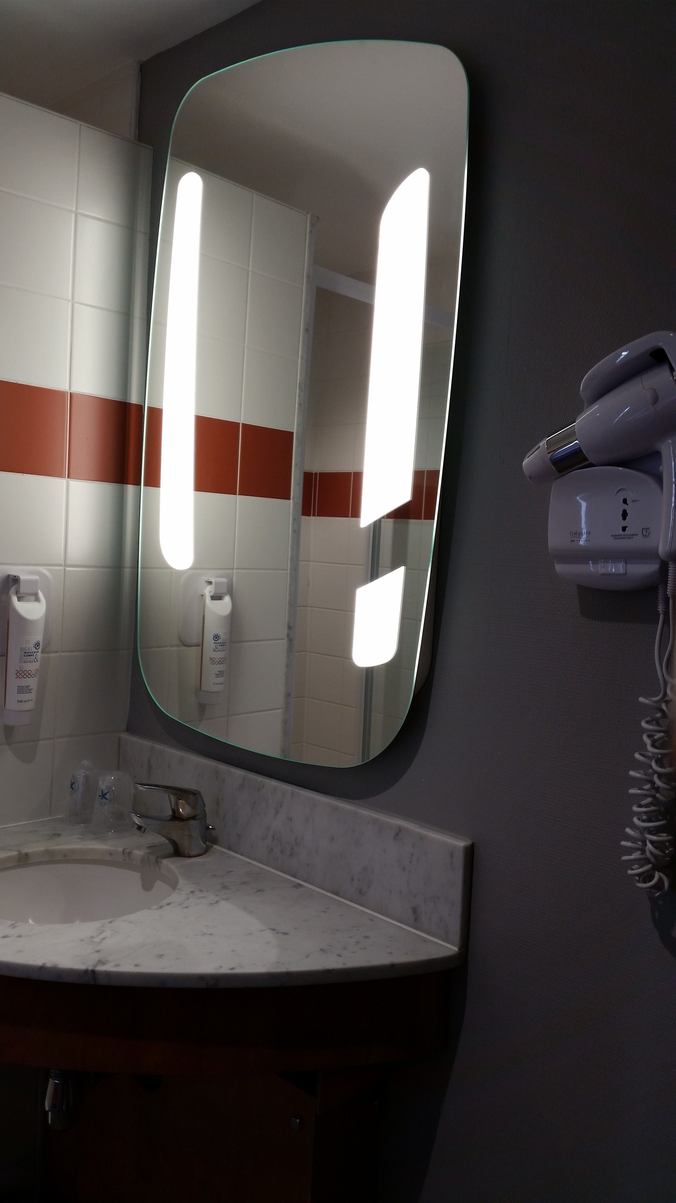 A bathroom with a large mirror, a sink, and a hairdryer on a wall-mounted charging station.