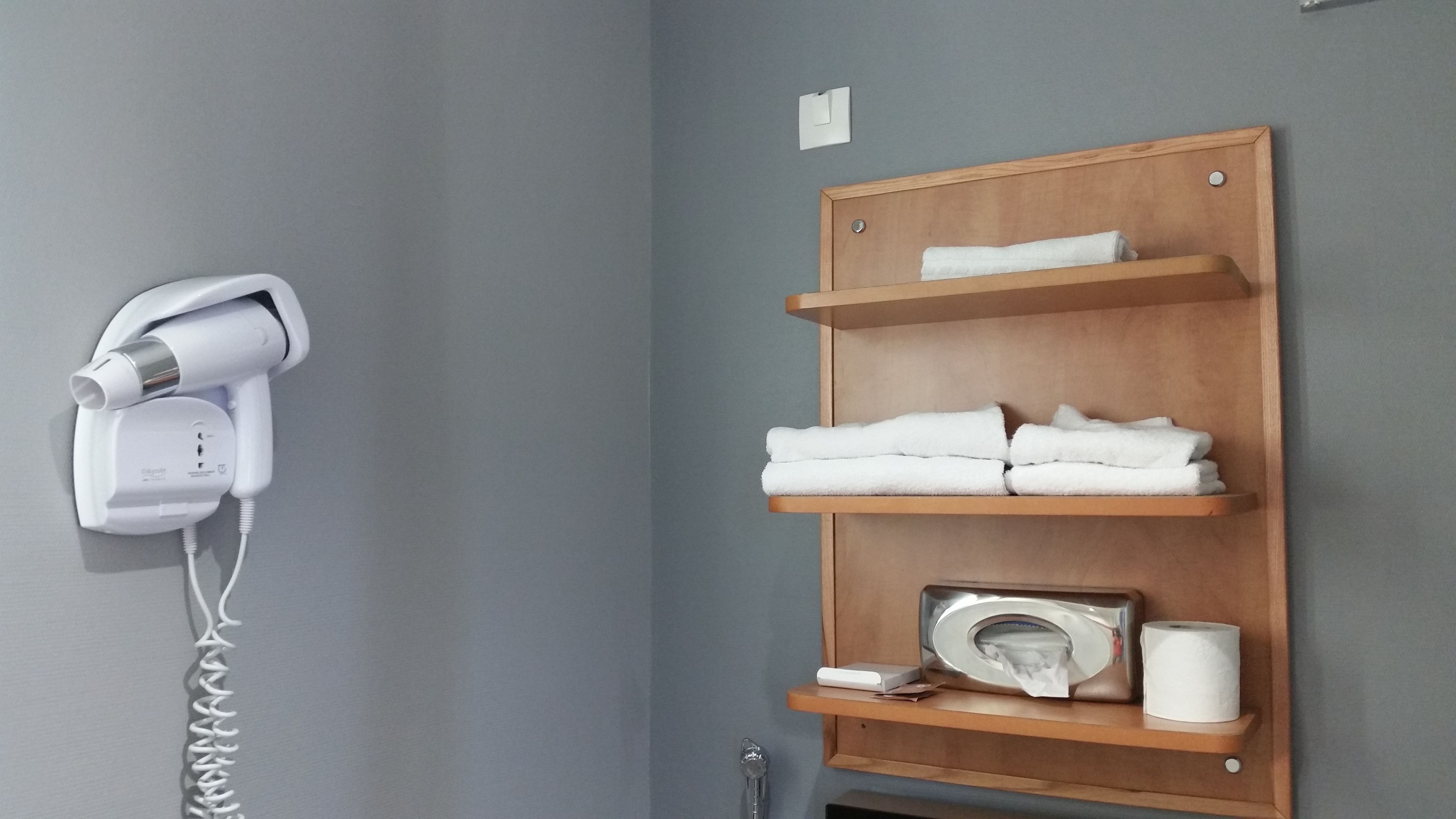 A hotel bathroom with a hairdryer, towels, a toilet paper holder, and a key.