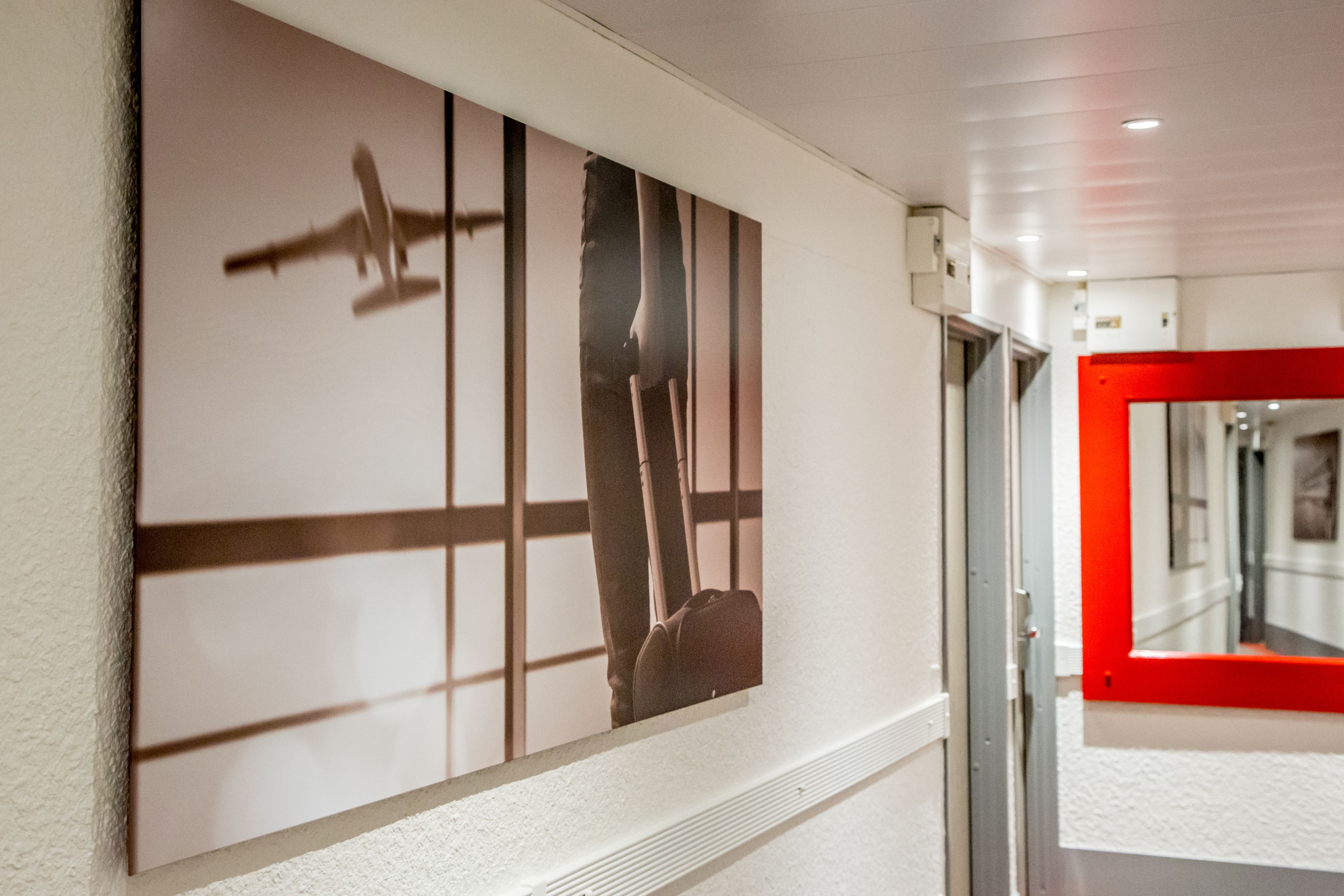 Un pasillo con una gran obra de arte en la pared que muestra una figura con maleta y un avión.