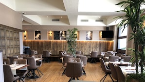 A restaurant with wooden flooring, modern furniture, and a large plant in the center.