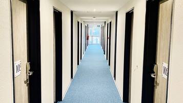 Pasillo de hotel con alfombra azul, puertas numeradas 103 y 102, y vista al vestíbulo al final.
