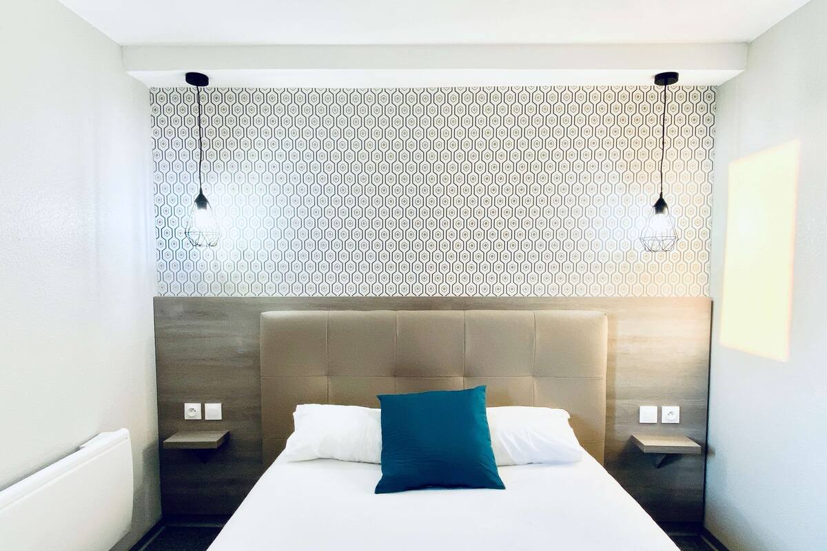 Une chambre d’hôtel moderne avec un grand lit, deux tables de chevet et un papier peint à motifs.