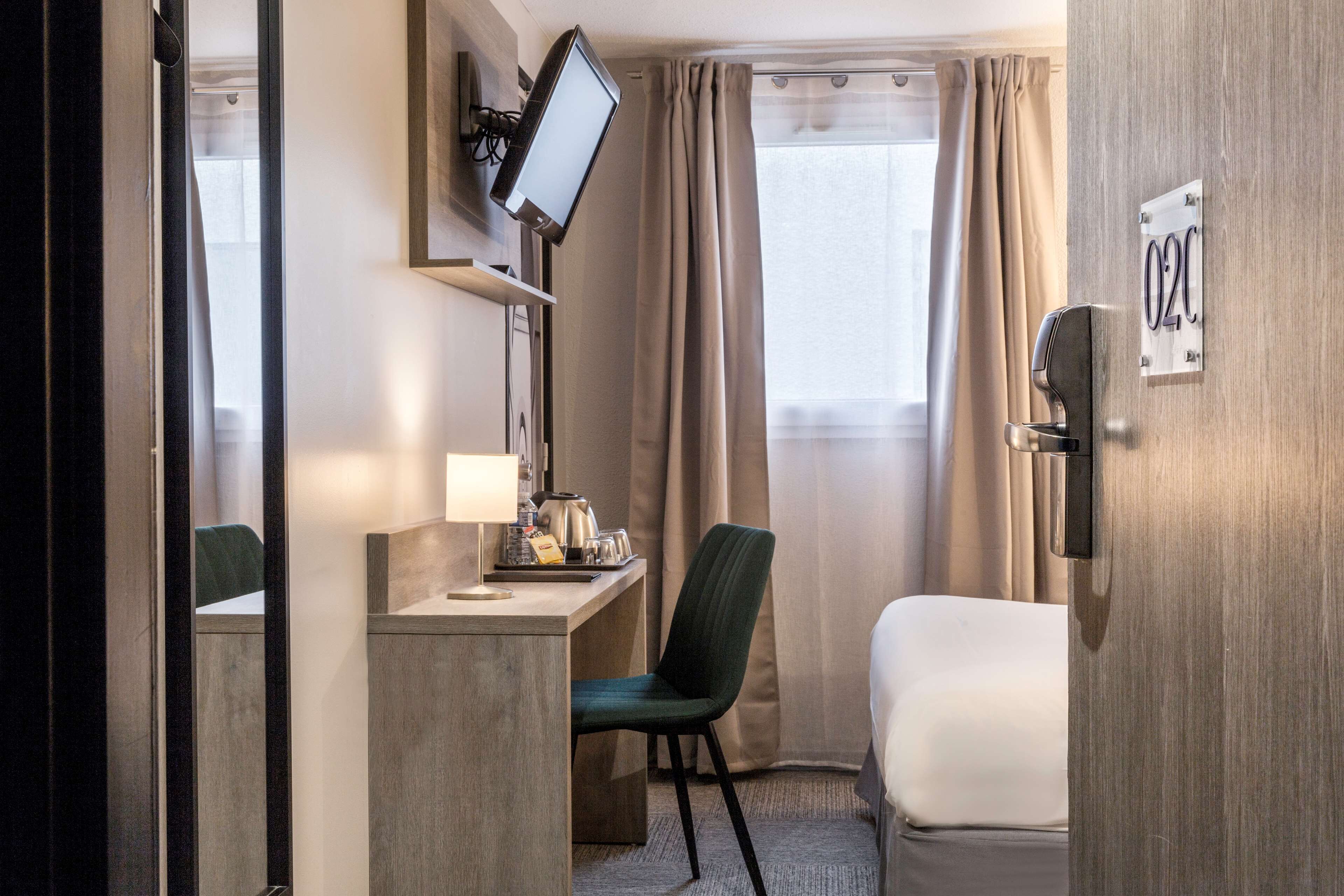 Quarto de hotel com escrivaninha, cadeira, cama, televisão e porta com um aviso.