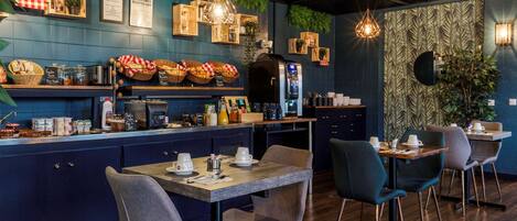 A restaurant with a blue wall, wooden counter, and green plants. There are tables and chairs for dining.