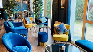 Un espace de détente moderne avec des sièges bleus et jaunes, une table basse en verre et un plafond orné de poutres apparentes et de lustres.
